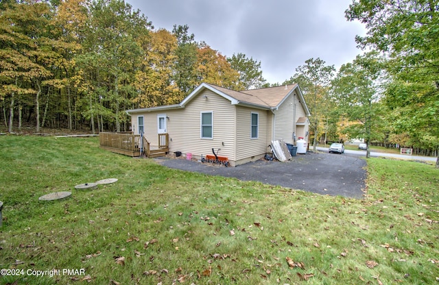 view of side of home featuring aphalt driveway, a yard, and a deck