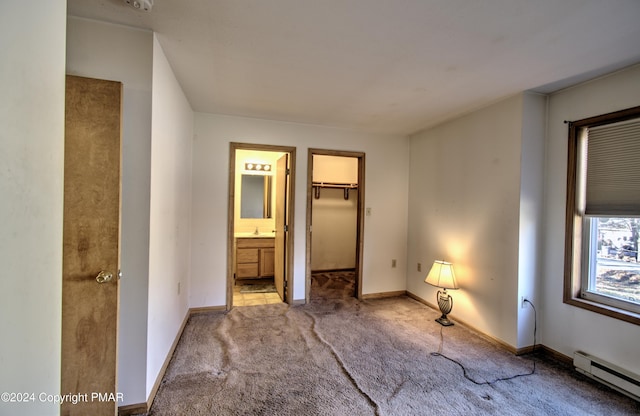 unfurnished bedroom with baseboards, ensuite bath, a spacious closet, carpet flooring, and a baseboard heating unit