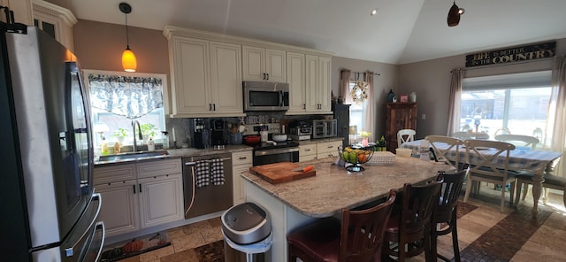 kitchen with a sink, light stone counters, backsplash, appliances with stainless steel finishes, and vaulted ceiling