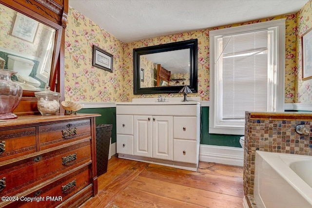 full bath featuring a wainscoted wall, a textured ceiling, wood-type flooring, and wallpapered walls