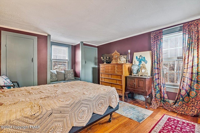 bedroom with a textured ceiling, ornamental molding, multiple windows, and wood finished floors