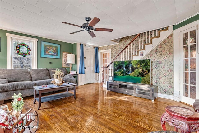 living room with ornamental molding, ceiling fan, wood finished floors, baseboards, and stairs