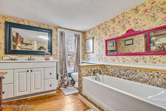 bathroom with a textured ceiling, toilet, wainscoting, wood-type flooring, and wallpapered walls