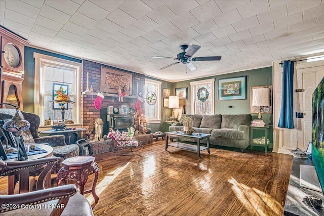 living room with ceiling fan, wood finished floors, a wood stove, and a healthy amount of sunlight