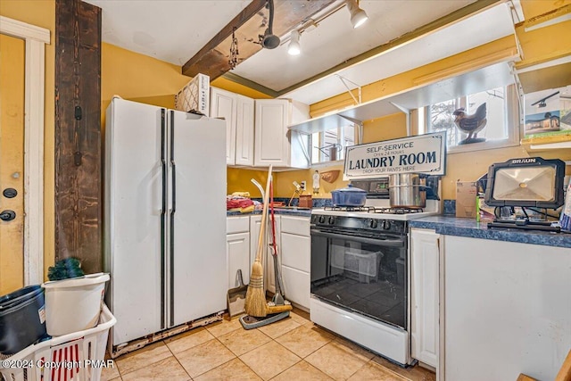 kitchen with light tile patterned floors, dark countertops, freestanding refrigerator, gas stove, and white cabinetry