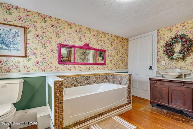 full bathroom featuring wallpapered walls, a textured ceiling, and wainscoting