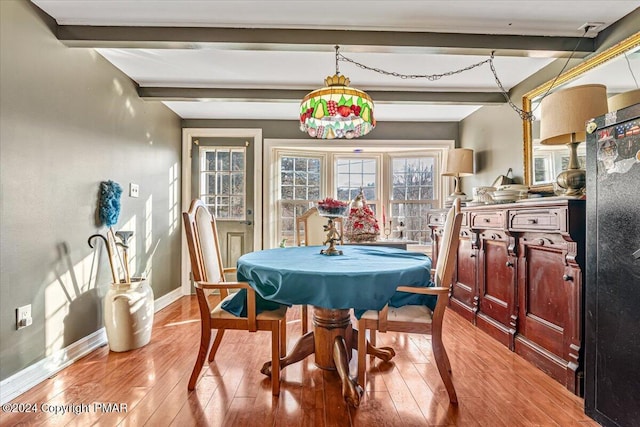 dining area with light wood-style floors, baseboards, and beamed ceiling