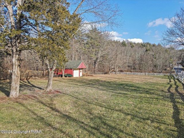 view of yard featuring an outbuilding, a forest view, and fence