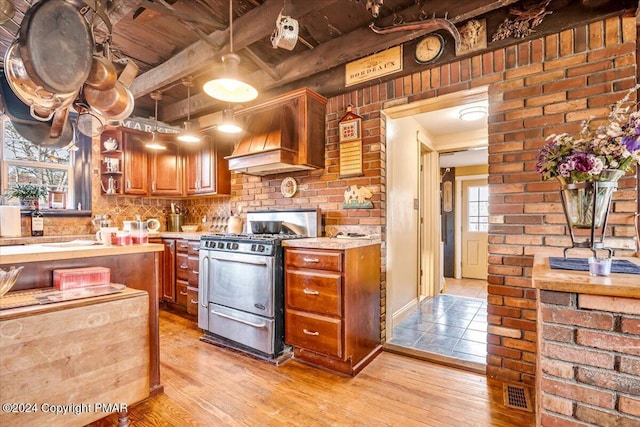 kitchen with stainless steel gas stove, light countertops, custom exhaust hood, and light wood-style flooring