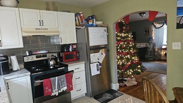 kitchen featuring under cabinet range hood, stainless steel appliances, arched walkways, and white cabinets