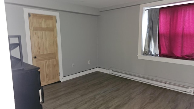 empty room with wood finished floors and a baseboard heating unit