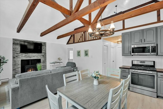 dining room with light wood finished floors, a chandelier, beamed ceiling, a fireplace, and high vaulted ceiling