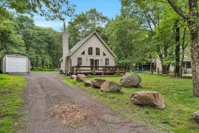 chalet / cabin featuring an outbuilding, gravel driveway, a chimney, a front yard, and a deck