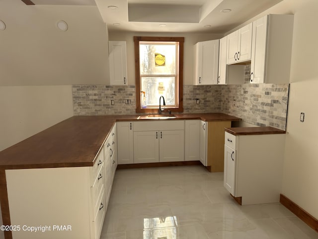 kitchen with a sink, white cabinets, tasteful backsplash, dark countertops, and a raised ceiling