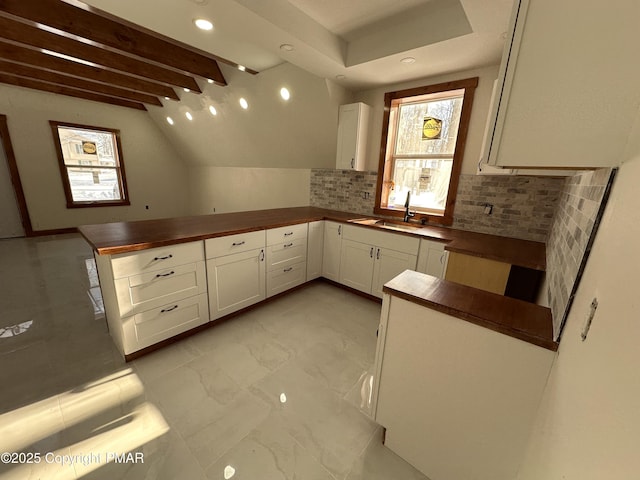 kitchen with decorative backsplash, white cabinets, a peninsula, marble finish floor, and a sink