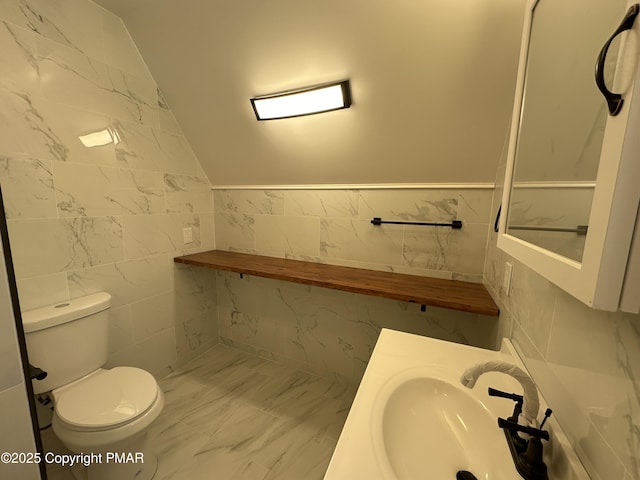 half bathroom featuring lofted ceiling, a sink, tile walls, and toilet