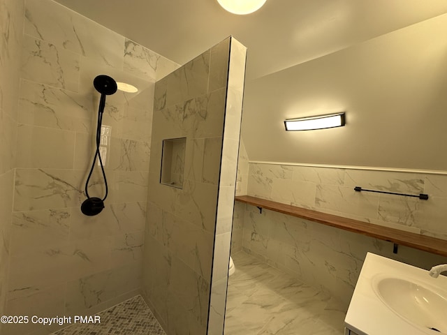 bathroom featuring a wainscoted wall, vanity, tile walls, marble finish floor, and a tile shower