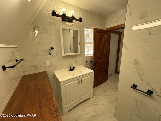 bathroom with lofted ceiling, marble finish floor, tile walls, and vanity