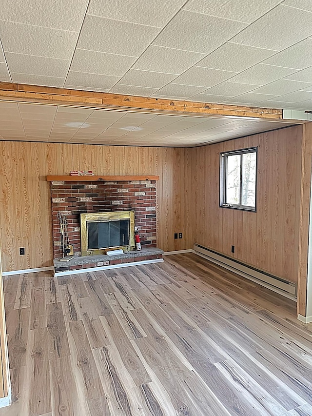 unfurnished living room featuring a brick fireplace, light wood finished floors, wood walls, and baseboard heating