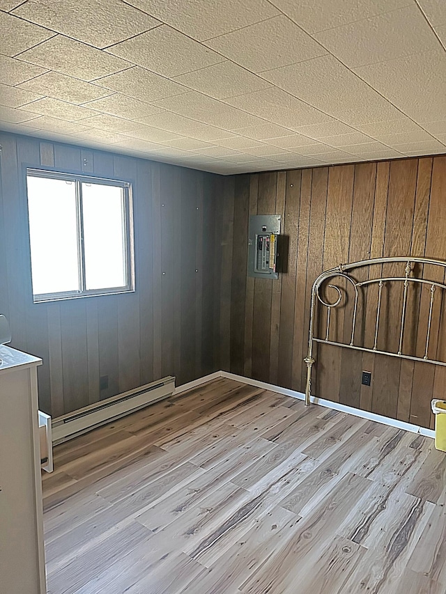 unfurnished room featuring electric panel, baseboard heating, wooden walls, and wood finished floors