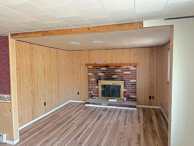 unfurnished living room featuring a brick fireplace, wood finished floors, baseboards, and wood walls