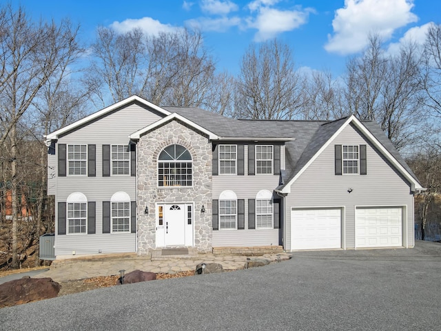 colonial home featuring aphalt driveway, stone siding, and roof with shingles