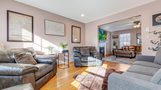 living area featuring baseboards, ceiling fan, recessed lighting, a fireplace, and light wood-style floors