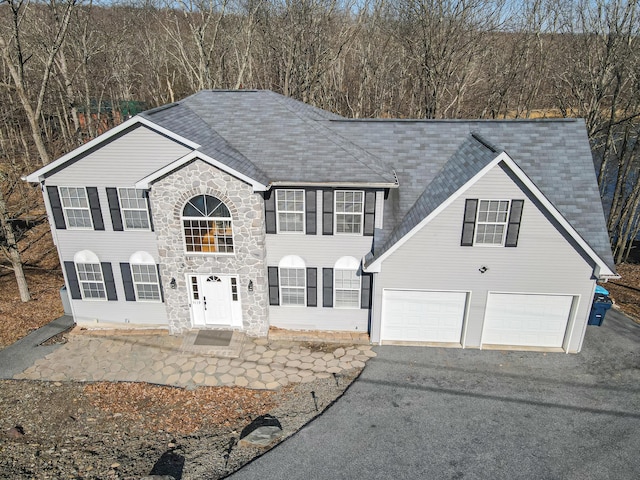 colonial home featuring stone siding, driveway, and a shingled roof