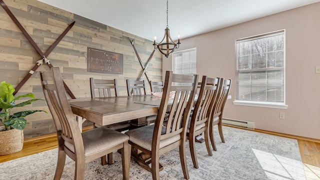 dining room with wooden walls, wood finished floors, baseboards, an inviting chandelier, and a baseboard heating unit