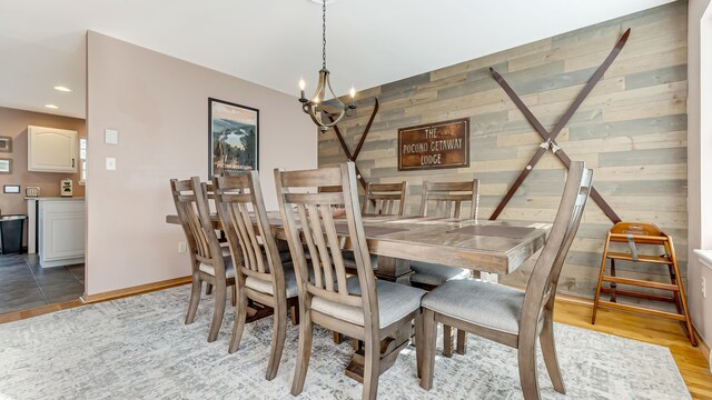 dining room with light wood finished floors, baseboards, wood walls, recessed lighting, and an inviting chandelier