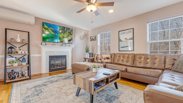 living area with a glass covered fireplace, plenty of natural light, a wall mounted AC, and a ceiling fan