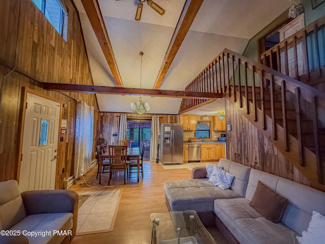 living area featuring beam ceiling, stairway, wood walls, light wood-type flooring, and ceiling fan with notable chandelier