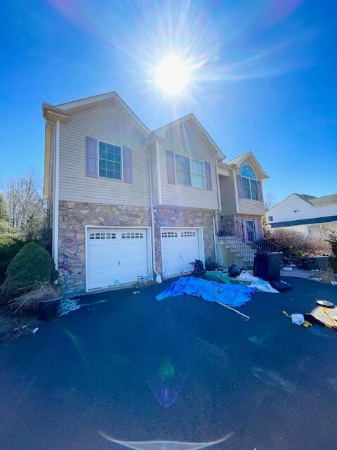 view of front facade with aphalt driveway, stone siding, and a garage