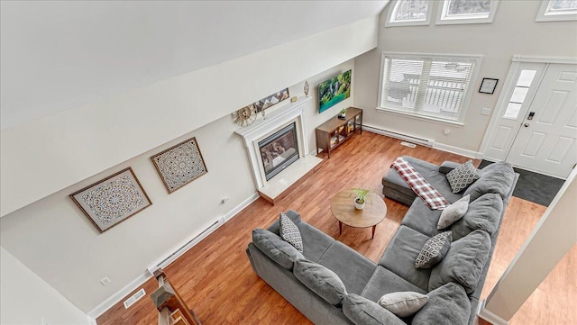 186 Brier Crest Rd, Blakeslee, PA 18610 - living area with a glass covered fireplace, wood finished floors, a baseboard heating unit, a baseboard radiator, and a towering ceiling