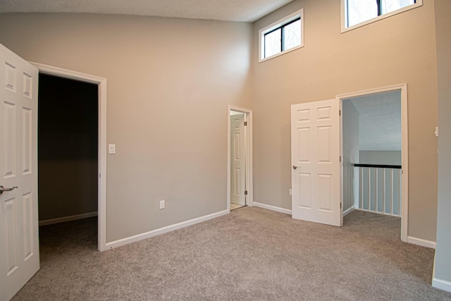 unfurnished bedroom featuring a walk in closet, carpet, a towering ceiling, and baseboards