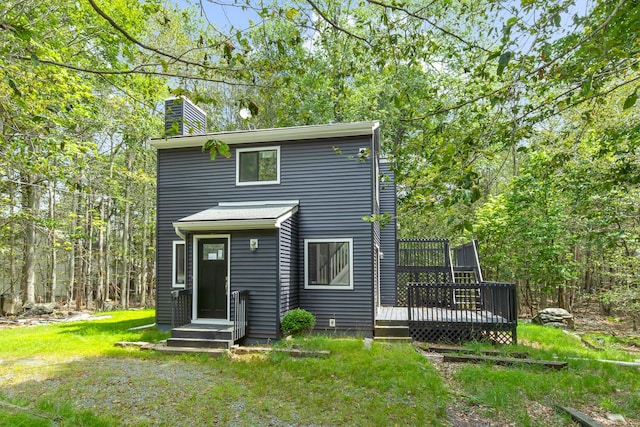 back of property with a chimney, a deck, and a lawn