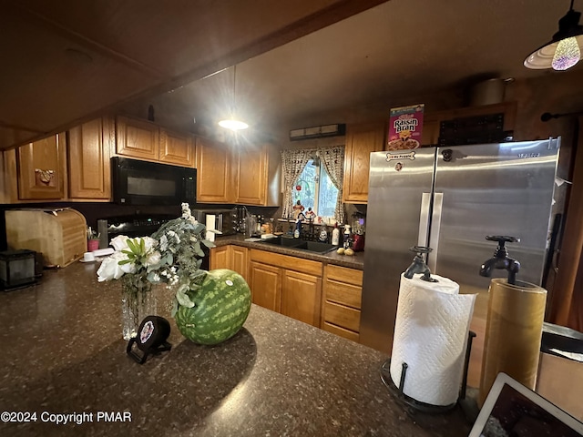 kitchen featuring freestanding refrigerator, black microwave, a sink, and dark stone countertops