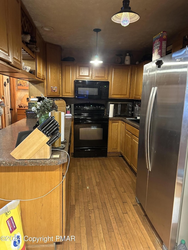 kitchen featuring open shelves, dark countertops, hanging light fixtures, light wood-type flooring, and black appliances