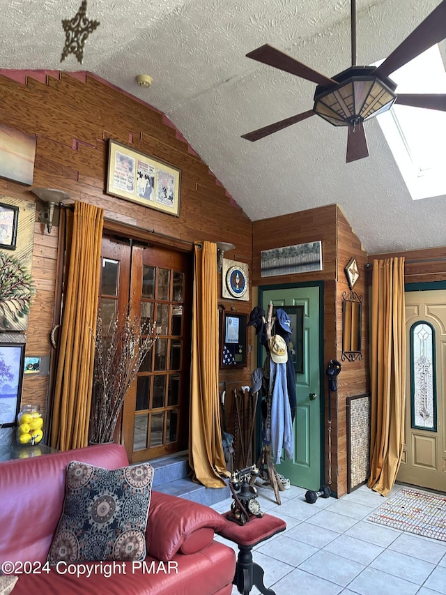 interior space with lofted ceiling with skylight, wooden walls, a ceiling fan, and a textured ceiling