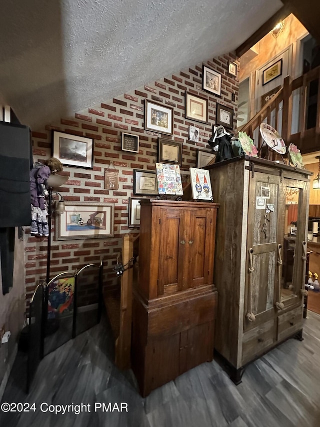 bar with lofted ceiling, a textured ceiling, brick wall, and wood finished floors