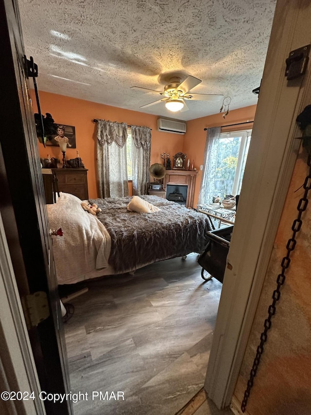 bedroom with a textured ceiling, an AC wall unit, wood finished floors, and a ceiling fan