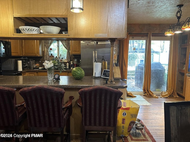 kitchen with dark countertops, a breakfast bar, wood finished floors, freestanding refrigerator, and a textured ceiling