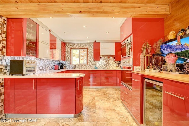 kitchen featuring beverage cooler, tasteful backsplash, red cabinets, beam ceiling, and a sink