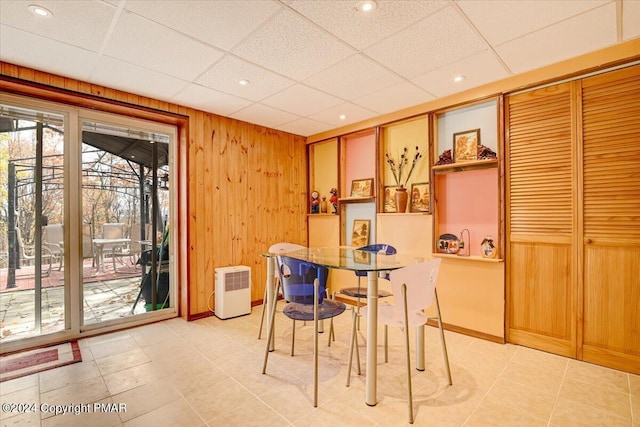 dining space featuring light tile patterned floors, a drop ceiling, recessed lighting, wood walls, and baseboards