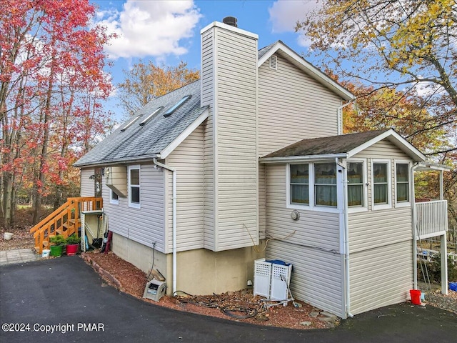 view of side of home featuring a shingled roof, a sunroom, and a chimney