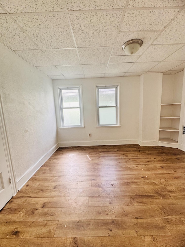 spare room featuring light wood-style floors, a paneled ceiling, and baseboards