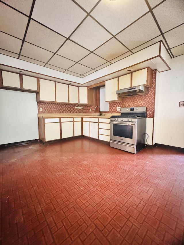 interior space featuring baseboards, a paneled ceiling, brick floor, and stainless steel gas stove