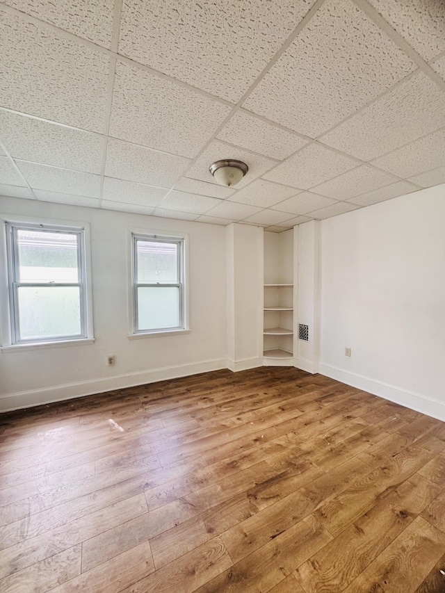 spare room featuring built in features, baseboards, a drop ceiling, and hardwood / wood-style floors
