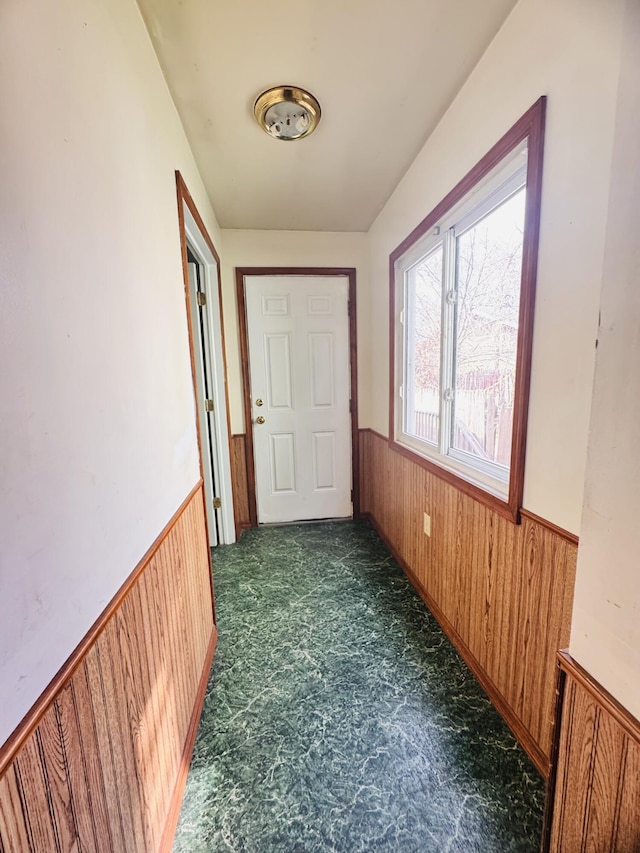 hall featuring dark colored carpet, wood walls, and a wainscoted wall