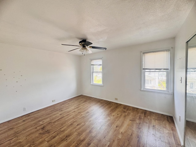 empty room with wood-type flooring, a ceiling fan, baseboards, and a textured ceiling